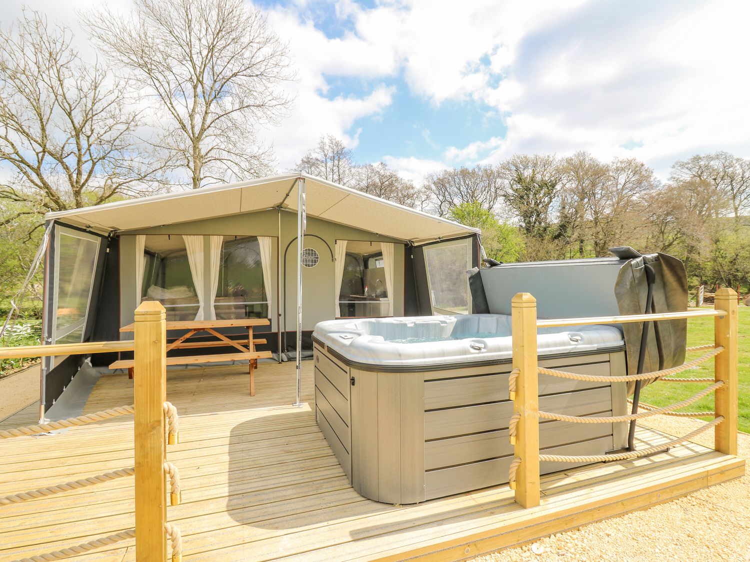 A wooden deck with hot tub and picnic table outside a tent in a wooded area at The Heron in Nantmel near Rhayader