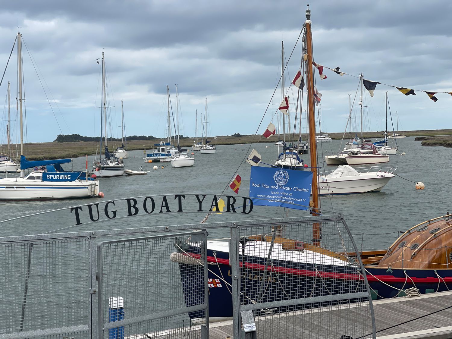 A harbor with moored sailboats and yachts behind a gate labeled Tug Boat Yard at Jolly Sailors Retreat - Wells next the Sea in Wells-Next-The-Sea