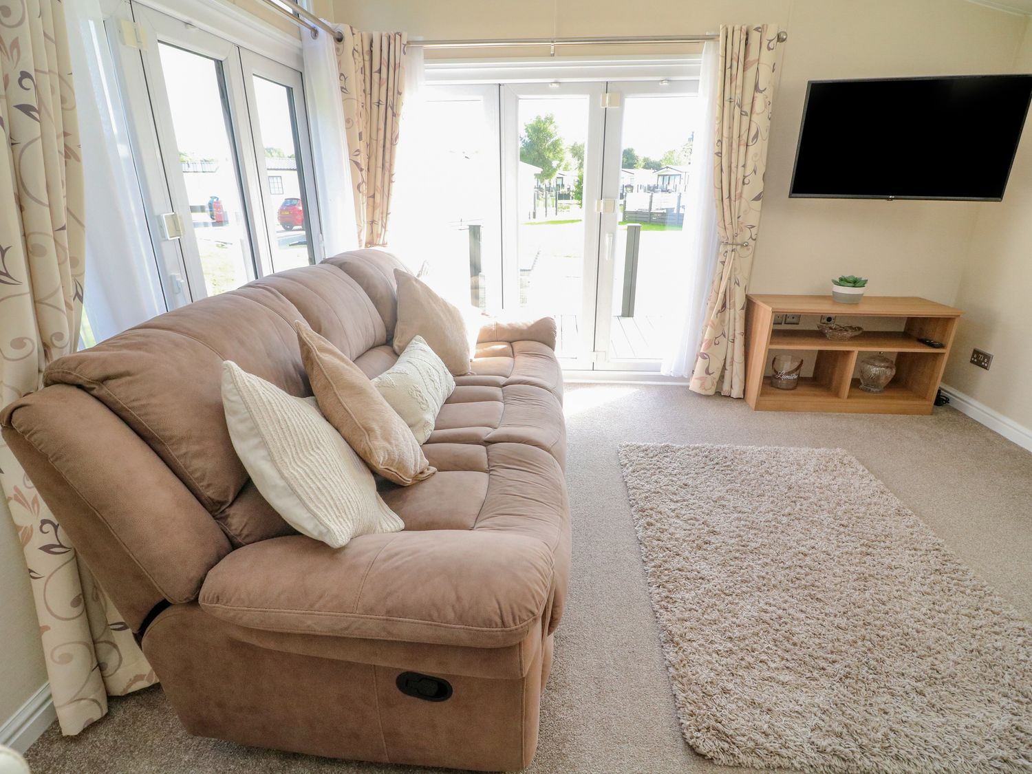 A living room with a brown sofa and cushions a rug a wall-mounted TV and a wooden TV stand at Number 15 in Carnforth