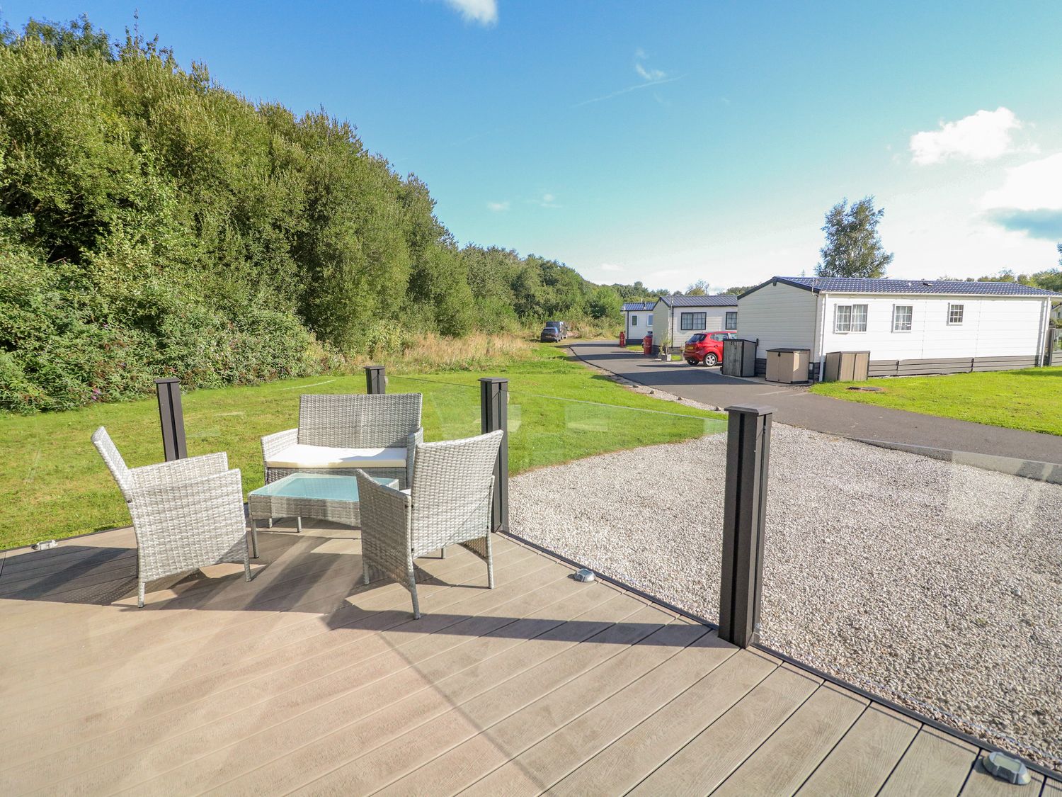 An outdoor seating area with chairs and a small table on a deck near mobile homes and greenery at Number 15 in Carnforth
