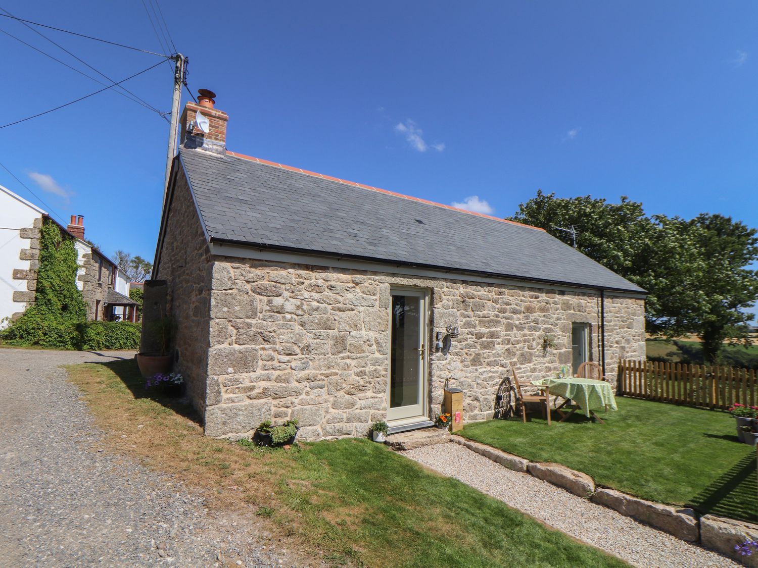 A stone cottage with a slate roof and a small garden with table and chairs at The Forge in Mawnan Smith