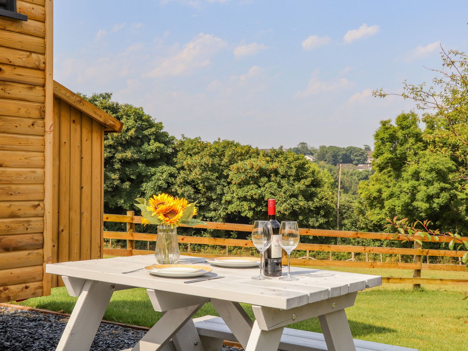 A picnic table with plates wine bottle glasses and flowers outside near wooden building and fence at Sunflower Sparnon Gate near Illogan