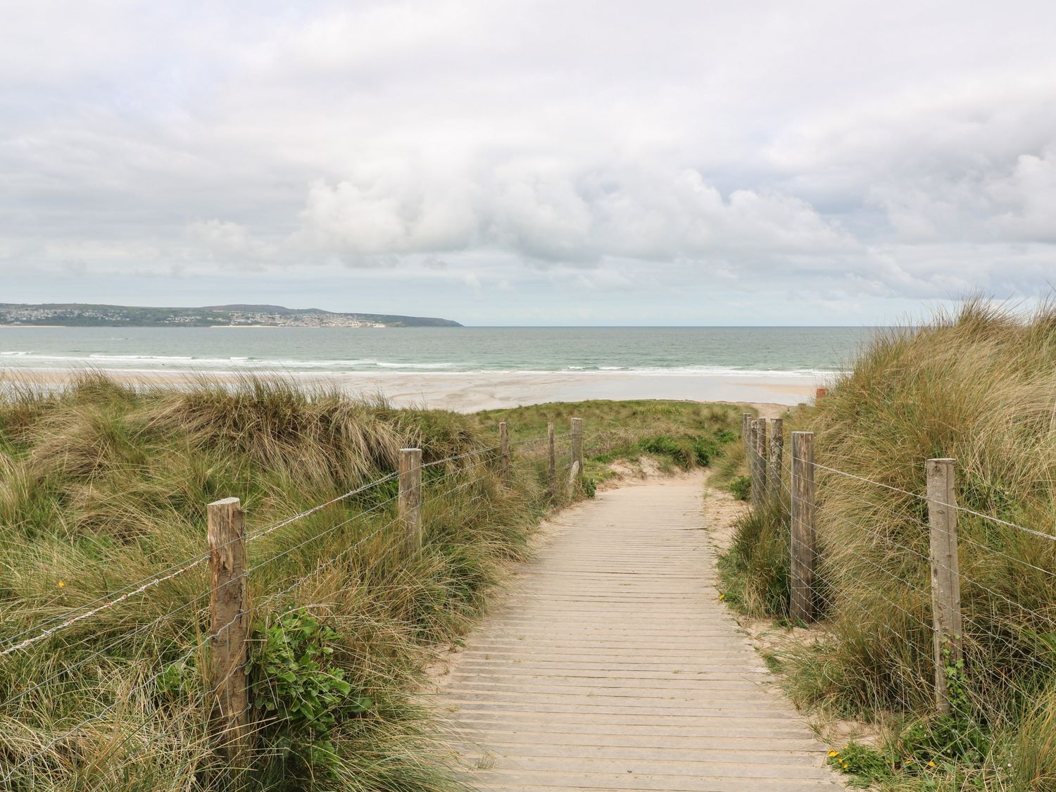 A wooden pathway between grassy sand dunes leading to a beach and ocean at Sunflower Sparnon Gate near Illogan