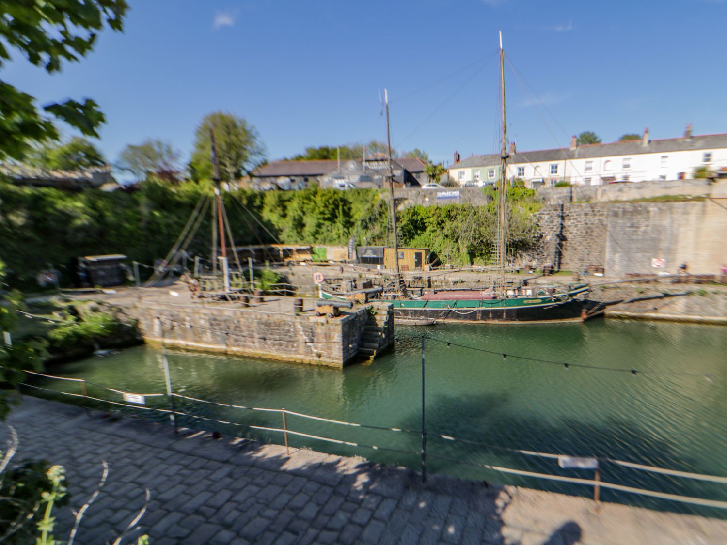 A dock with sailboats moored in the water near stone buildings and cobblestone path at Quay House in Charlestown