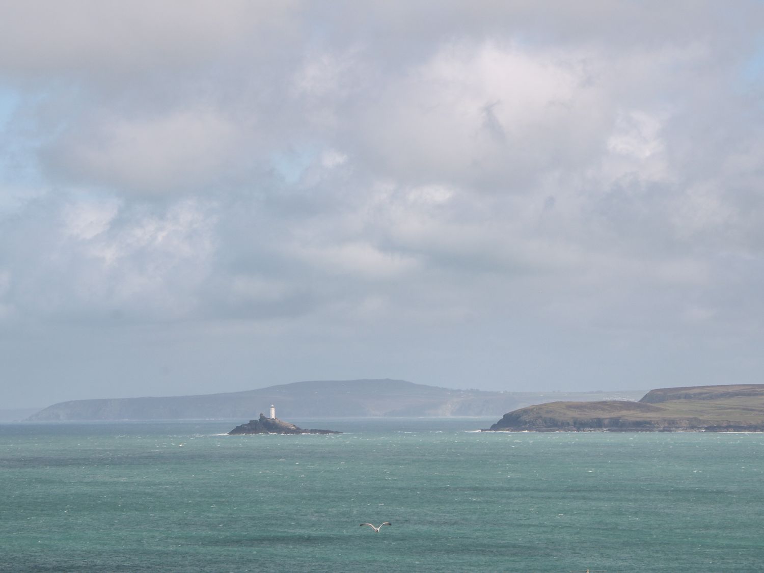 A lighthouse on a small island in the sea with distant hills and cloudy sky at Rose in Illogan
