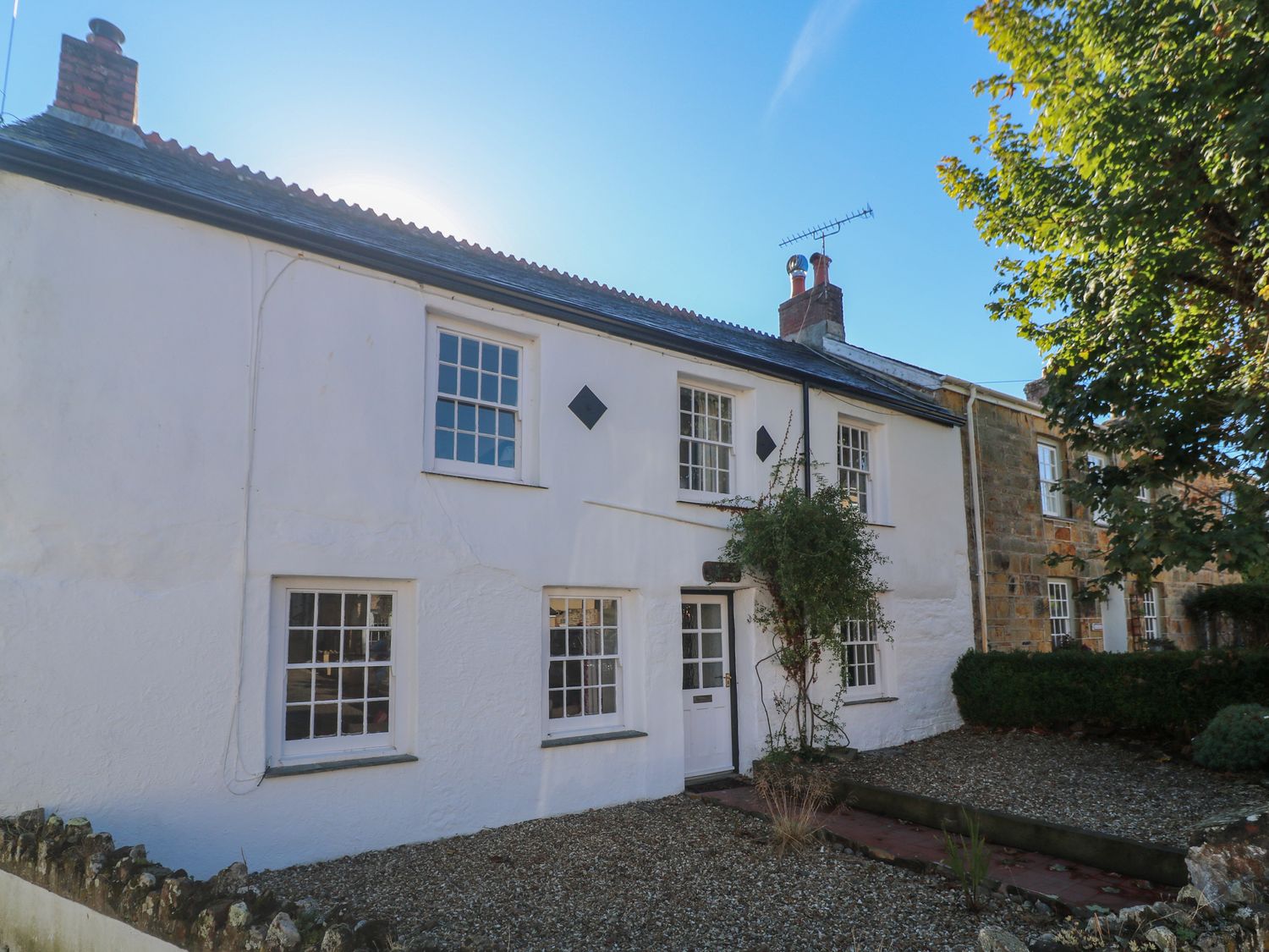 A white two-story house with multiple windows a white door gravel in front and a tree on the side at Kimberley House in St Columb Minor