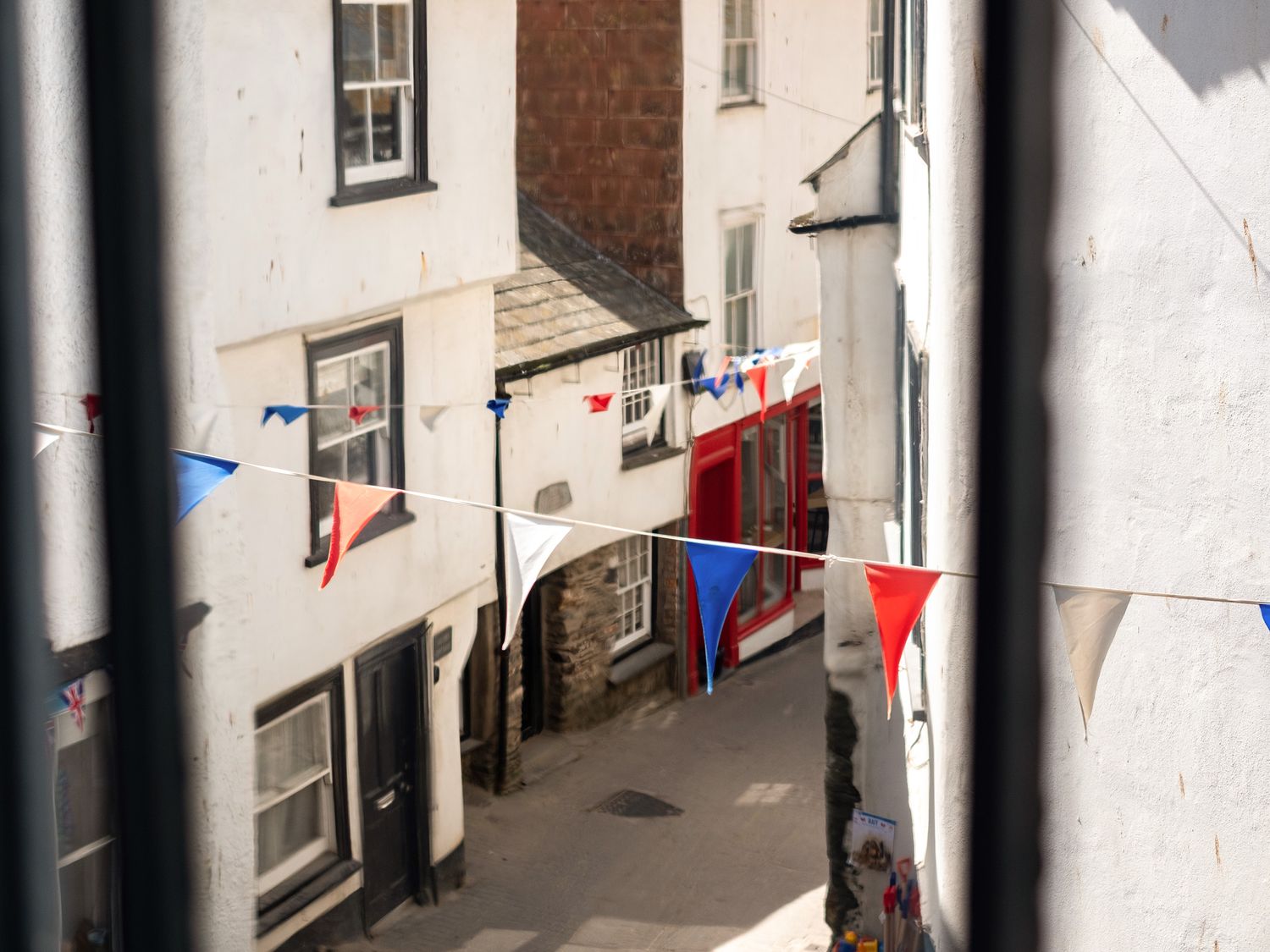 A narrow street with string bunting in red white and blue between white buildings at Pibbies in Port Isaac