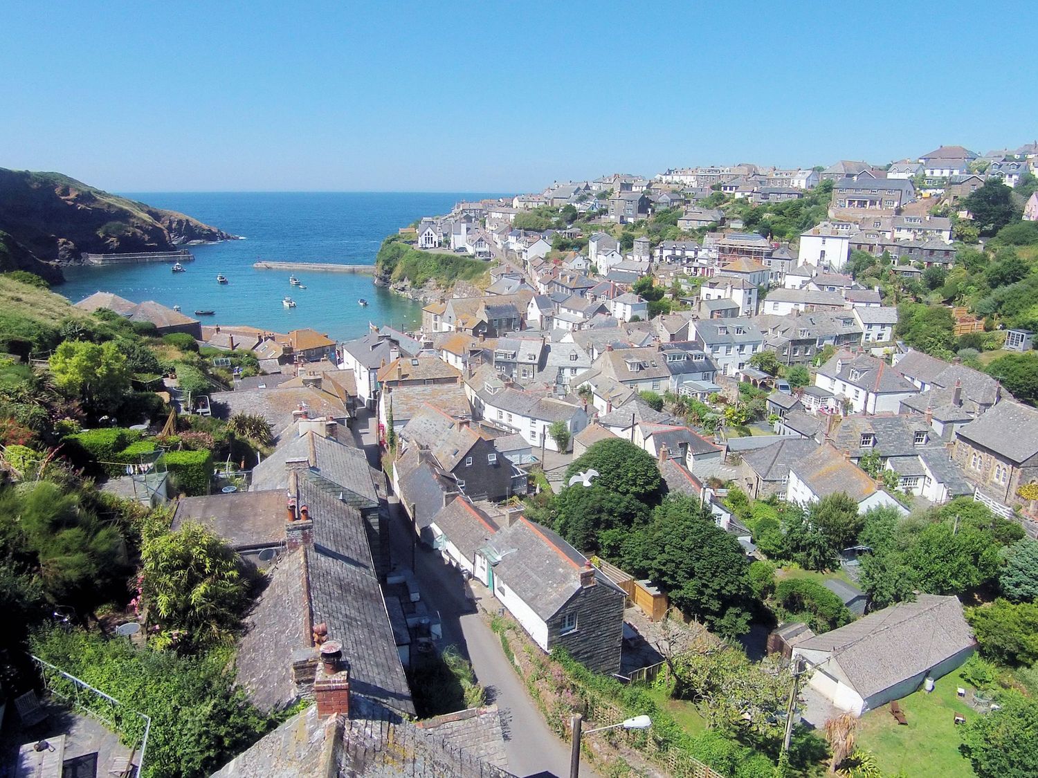 A coastal village with houses, greenery, and a harbor with boats at Pibbies in Port Isaac