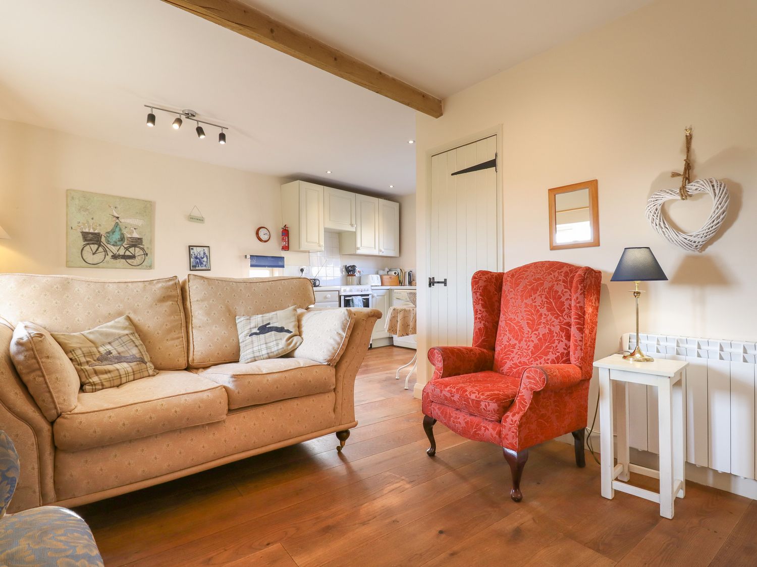 A living room with a beige sofa and red armchair next to a white side table and lamp at The Old Dairy in Colyton