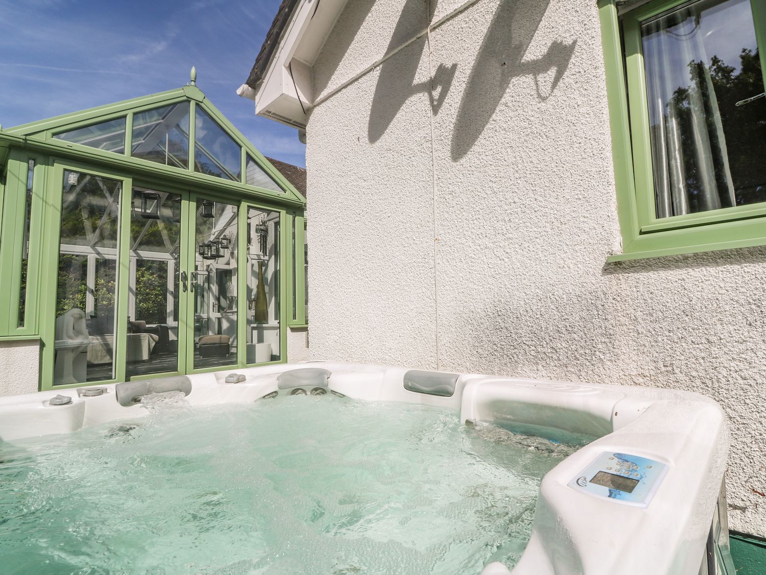A bubbling hot tub outside next to a white wall with a green window and a green conservatory at Cornerstone in Penzance