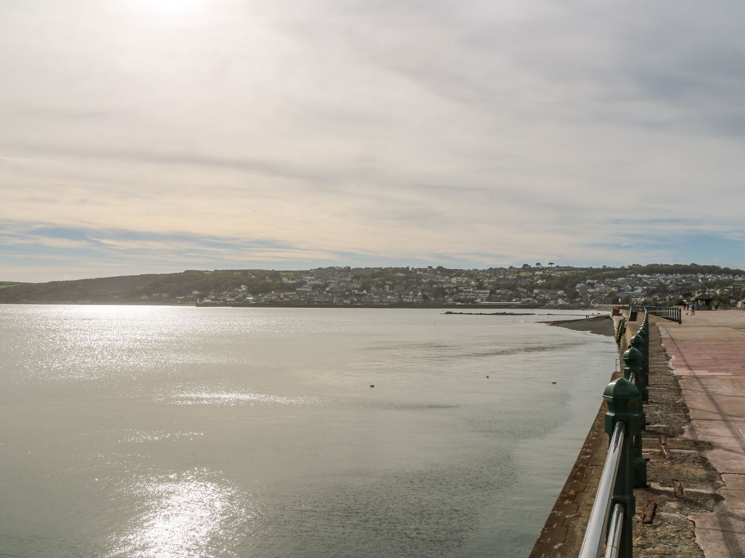 A waterfront promenade with railing and a view of a coastal town across the water at Cornerstone in Penzance
