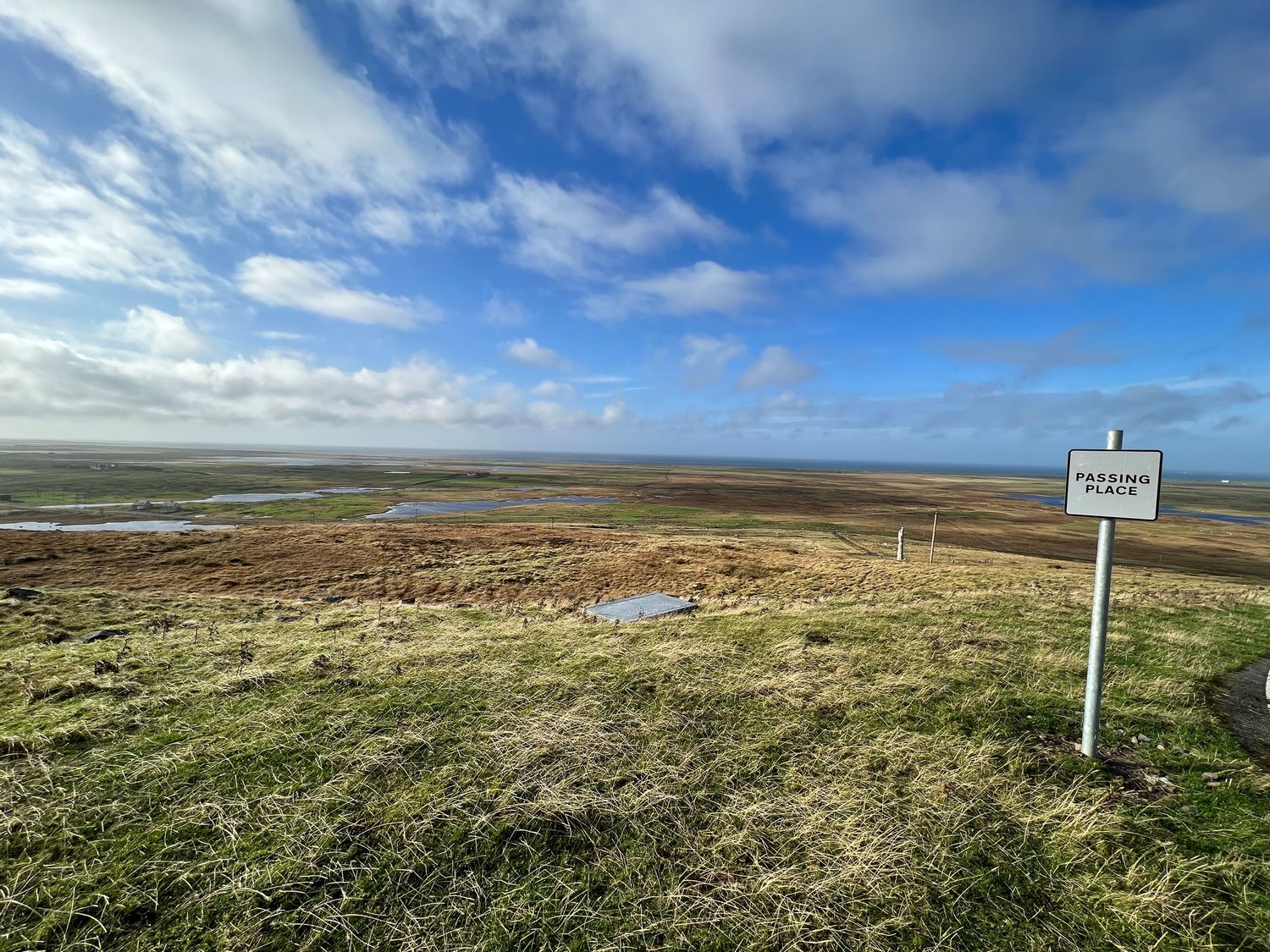 A grassy landscape with a passing place sign and a cloudy blue sky at Airigh nam Fiadh in Geirinis near Creagorry