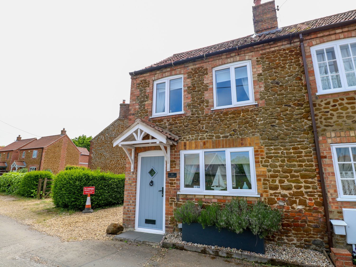 Exterior view of a stone and brick two-story house with a light blue front door and white framed windows at Herbies Cottage in Snettisham