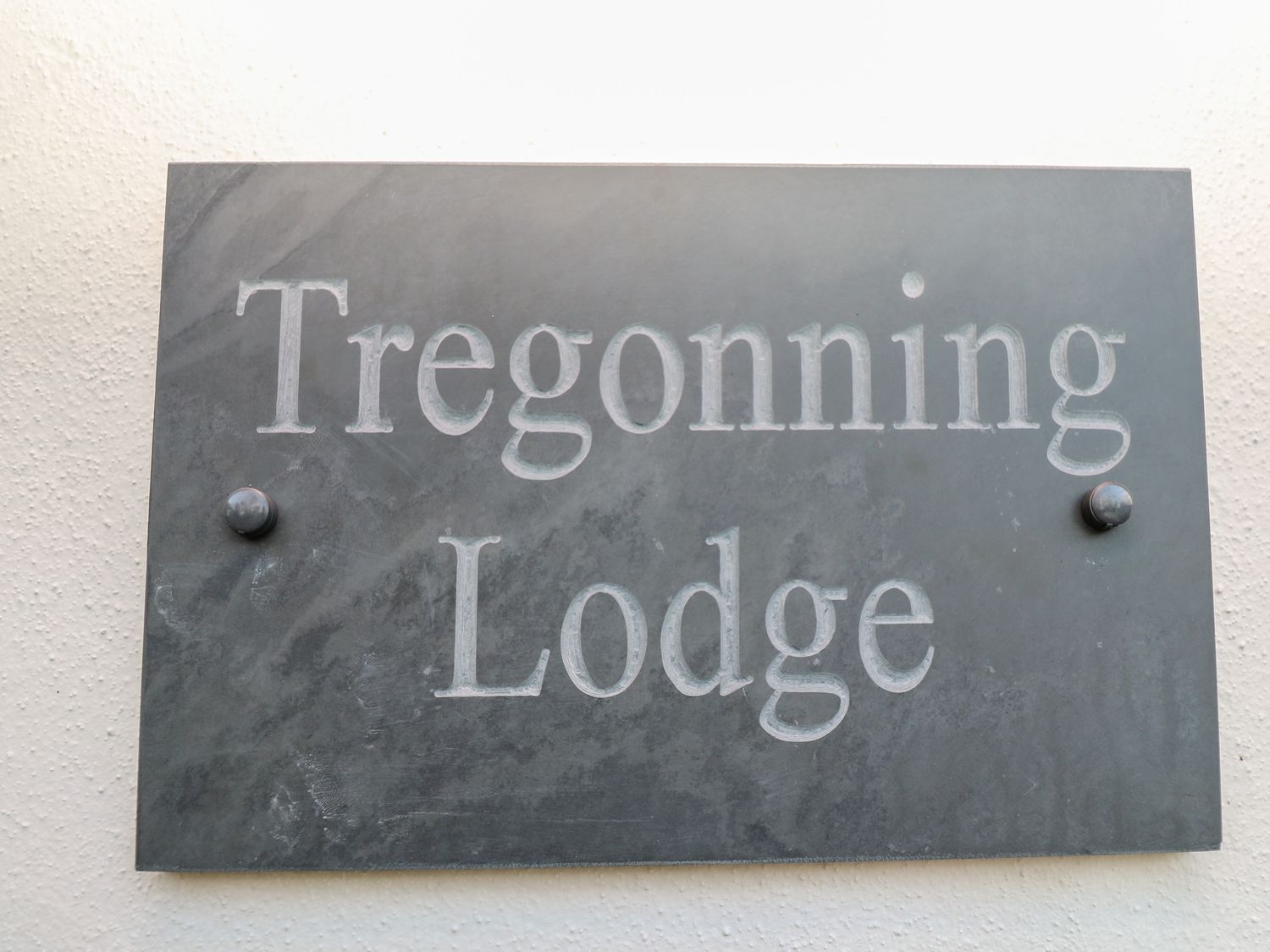 A gray stone plaque with the text Tregonning Lodge mounted on a white wall at Tregonning Lodge in Ashton near Rosudgeon