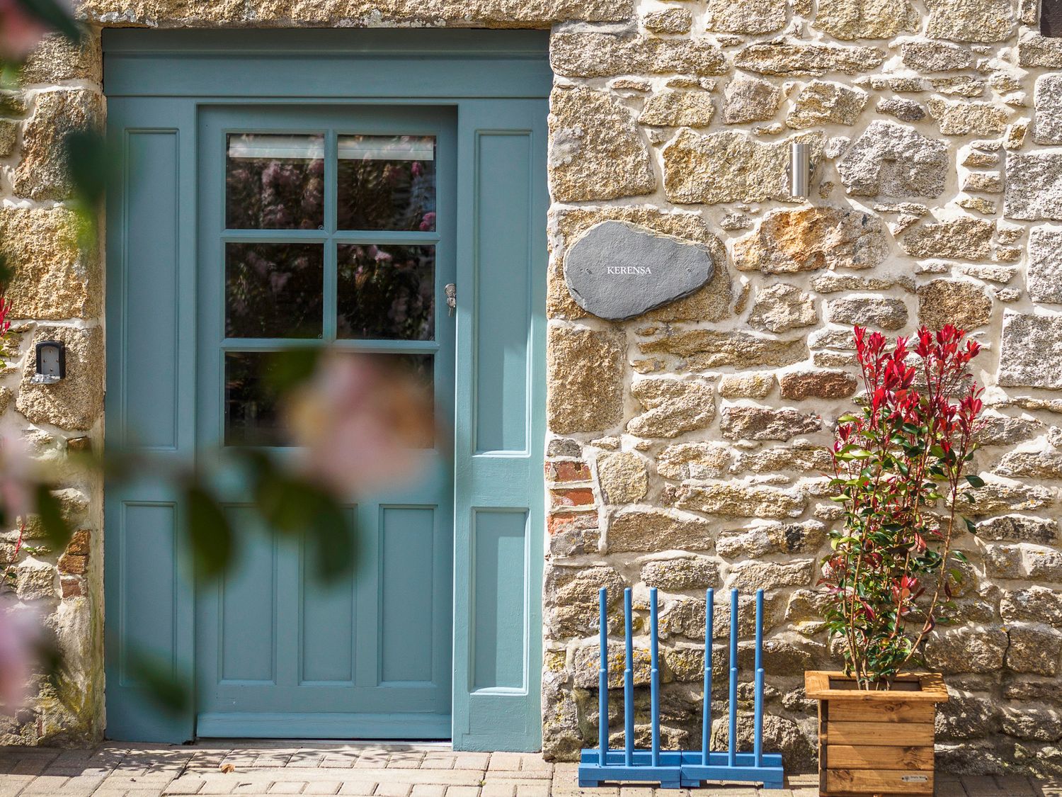 A blue door set in a stone wall with a plant in a wooden pot and a blue croquet set at Kerensa in Mawnan Smith Near Falmouth