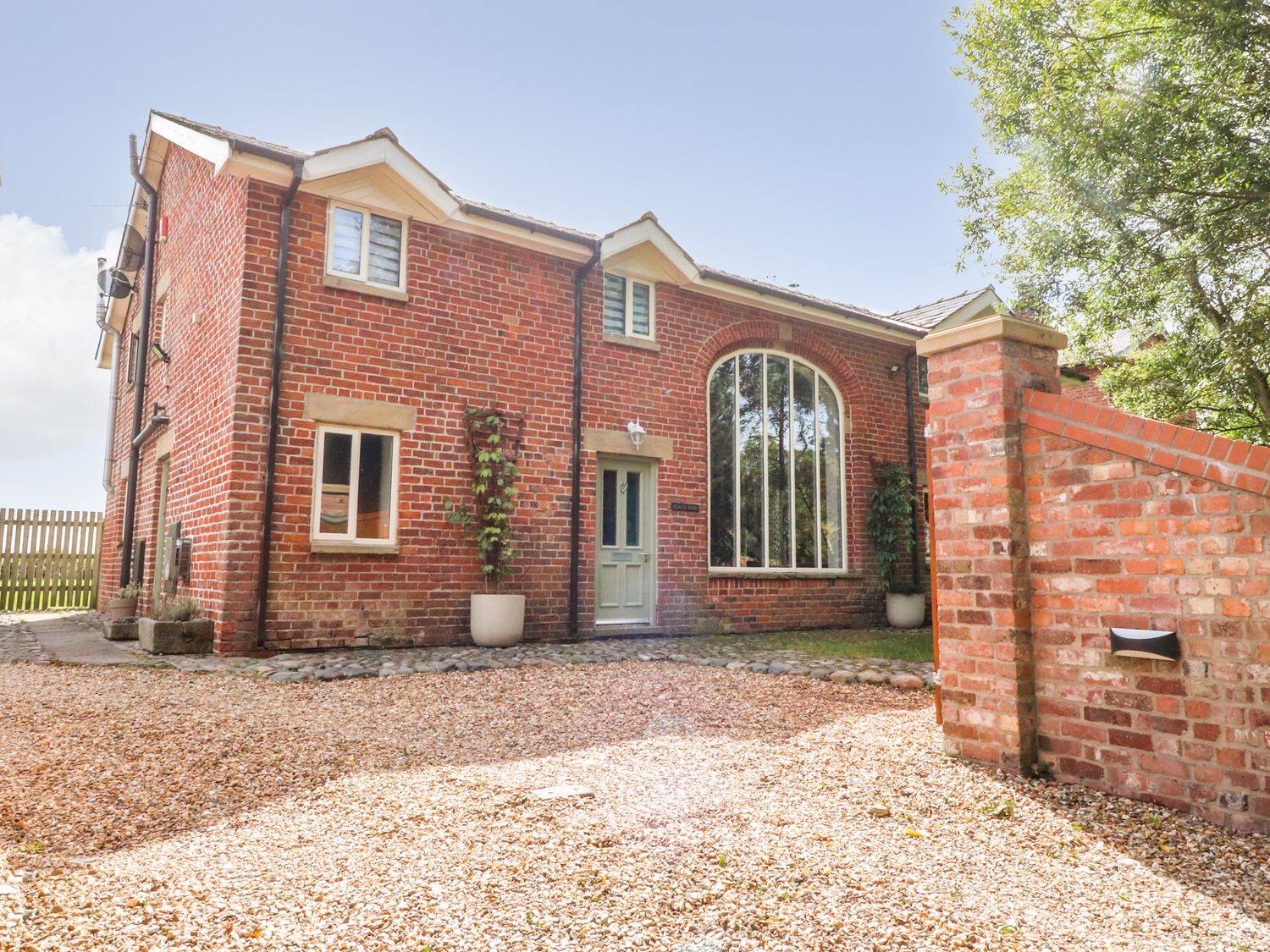 A brick house with a gravel driveway and large arched window at Noah's Barn in Hambleton Lancashire