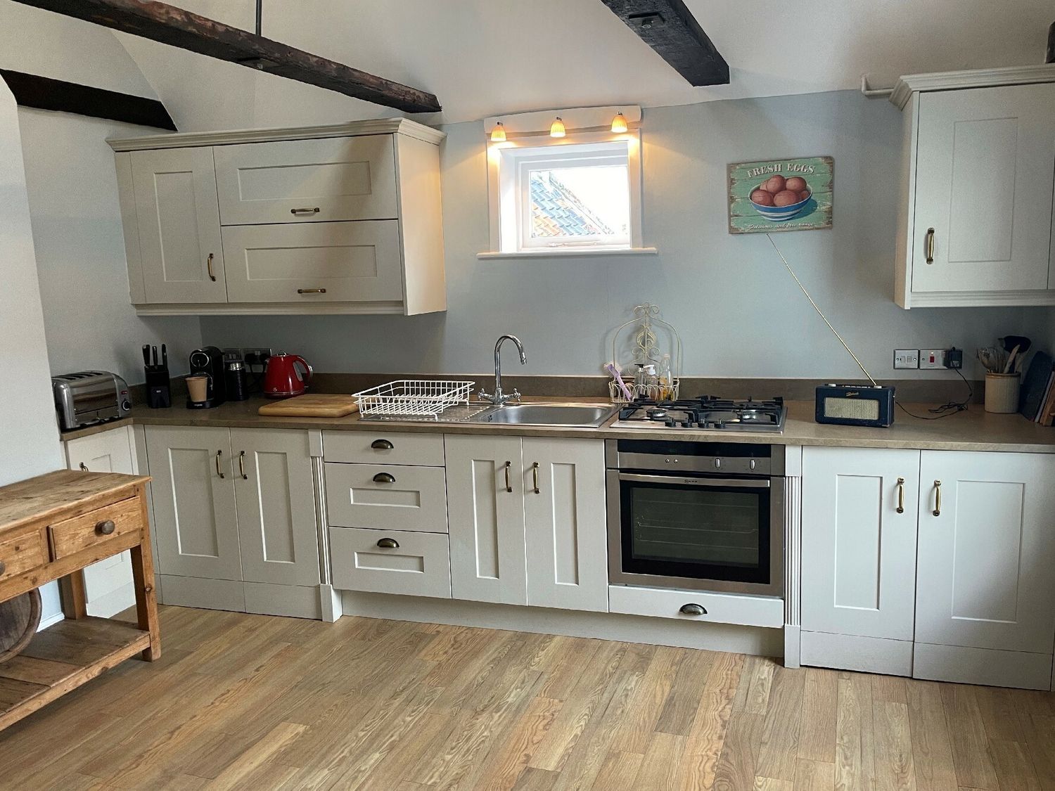 A kitchen with white cabinets a stainless steel oven a gas stove a sink a toaster kettle coffee maker and a wooden table at Walton House Southwold