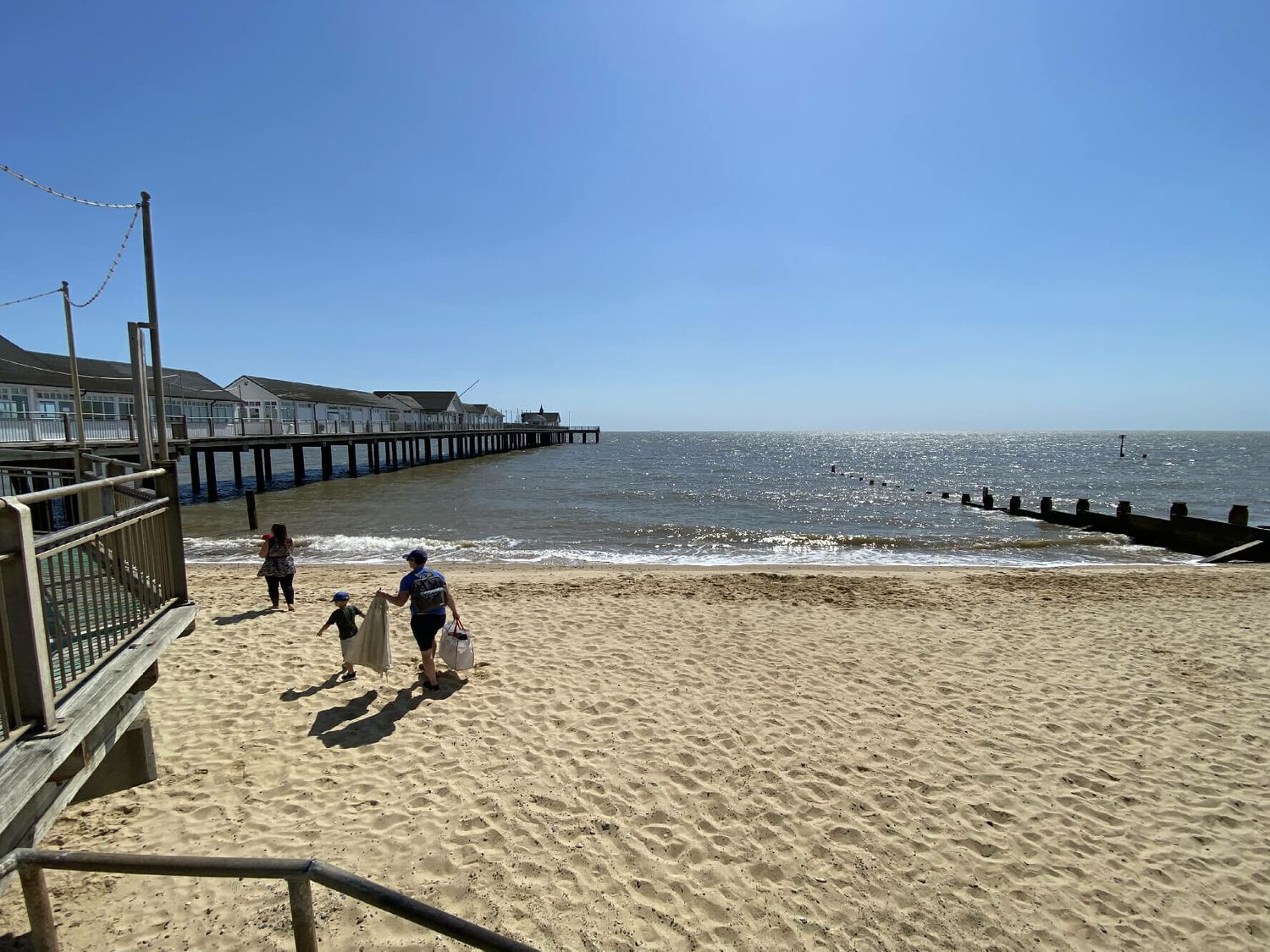 A sandy beach with three people walking near the water and a long pier extending into the sea at Walton House Southwold