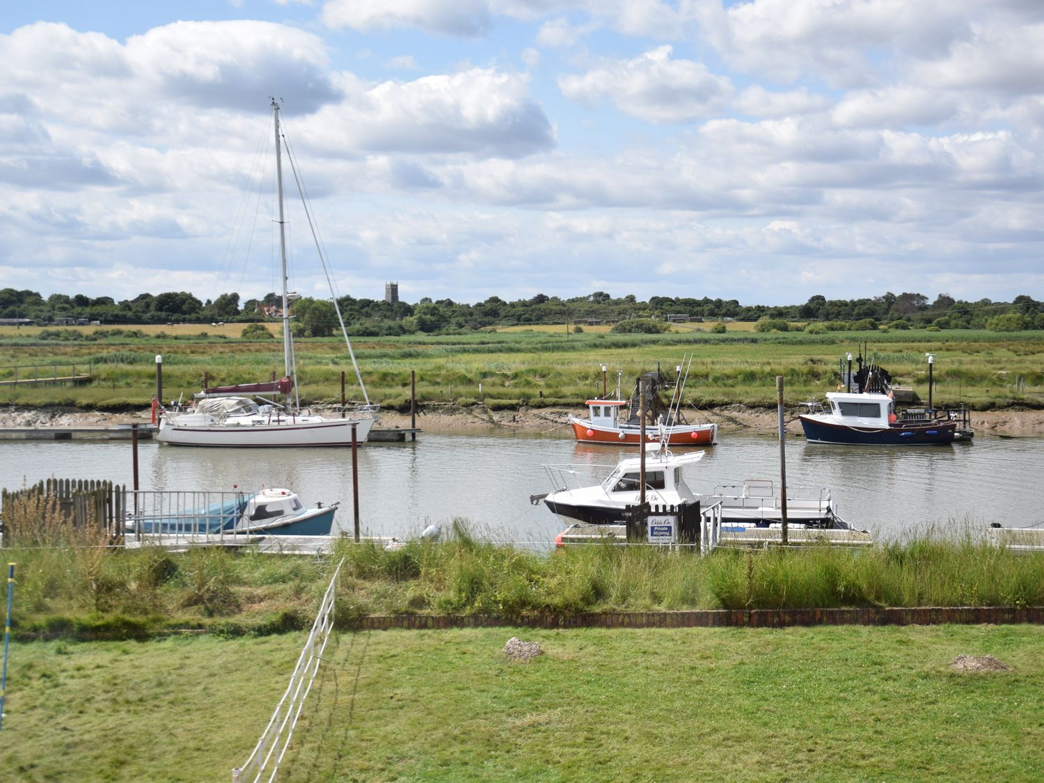 A river with boats docked by grassy banks and a church tower in the background at 5 Blackshore Southwold