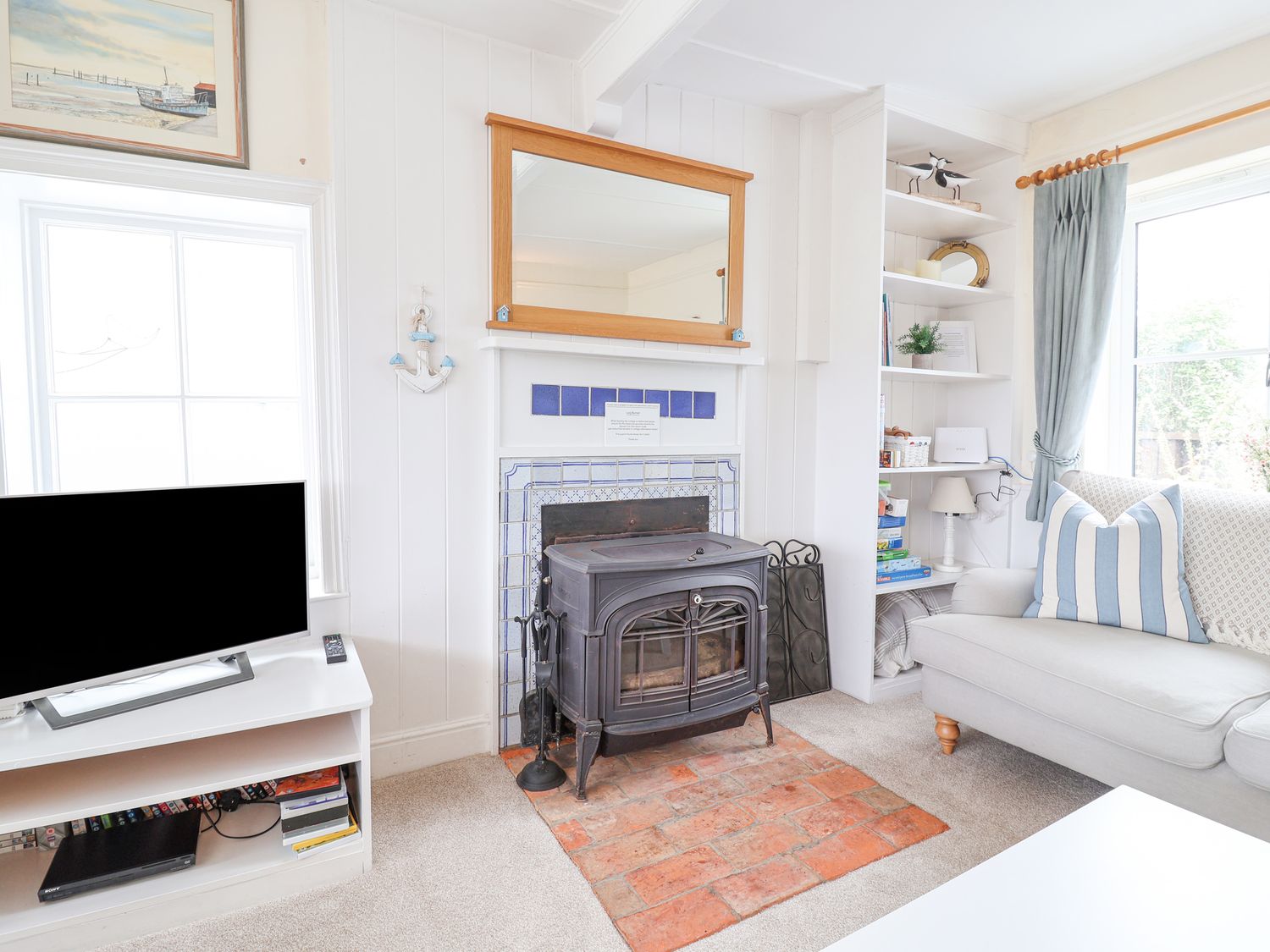 A living room with a wood stove fireplace sofa with striped pillow and a television on a white stand at 5 Blackshore Southwold