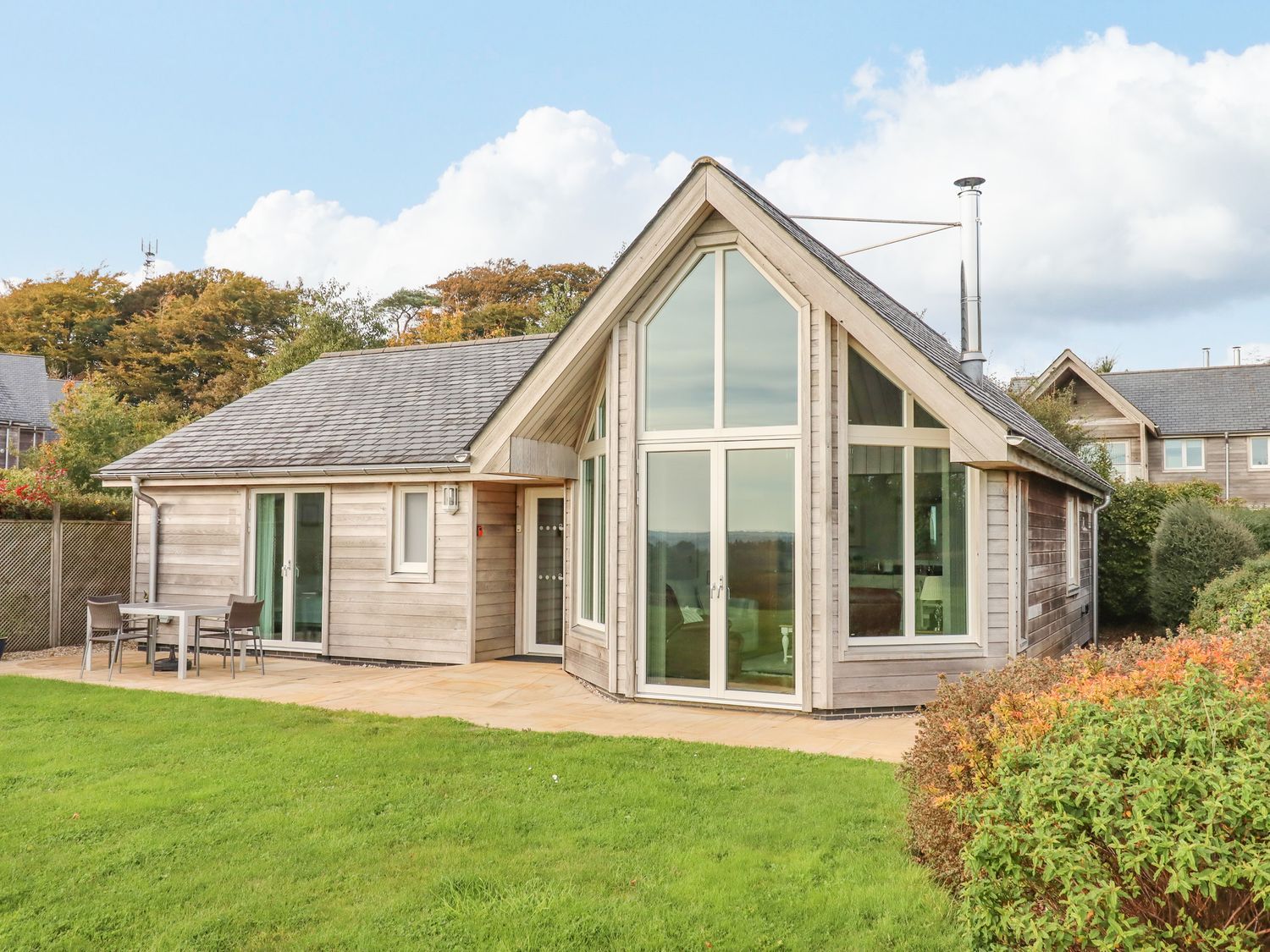 A wooden house with large windows and a garden with outdoor furniture at Swandown 11 The Cygnet in Cricket St Thomas