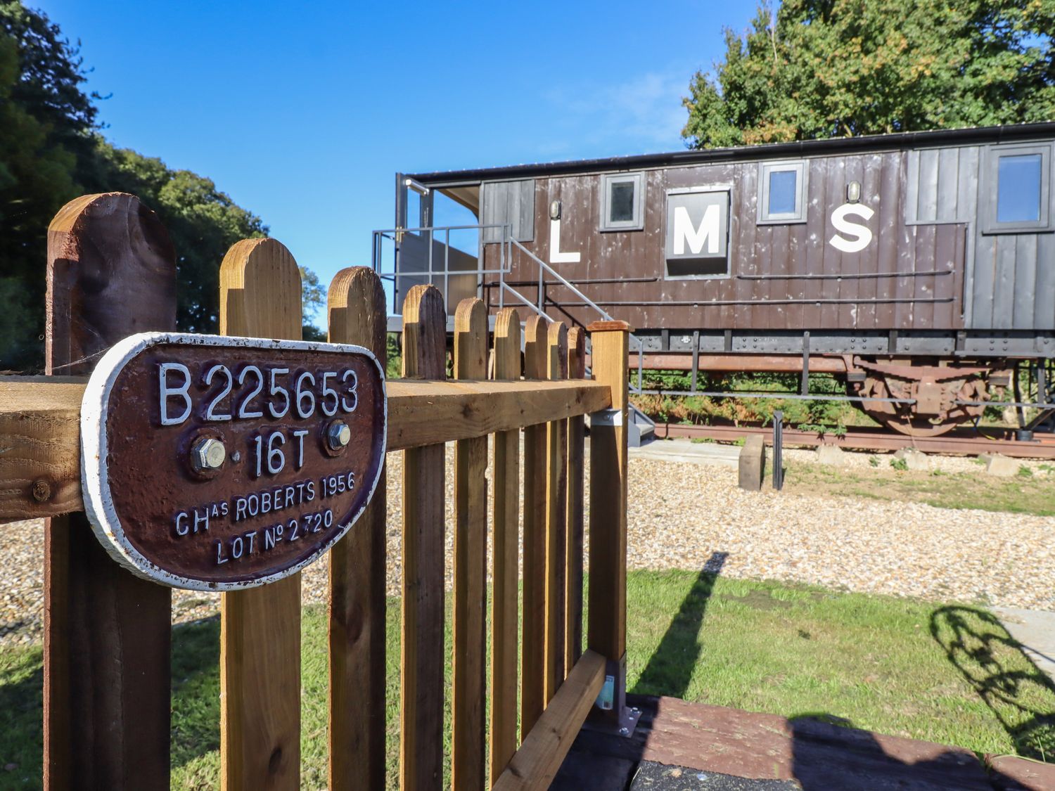 A wooden fence with a metal plate and a vintage railway carriage behind at The Brake Wagon at High Barn Heritage Greenstead Green near Halstead