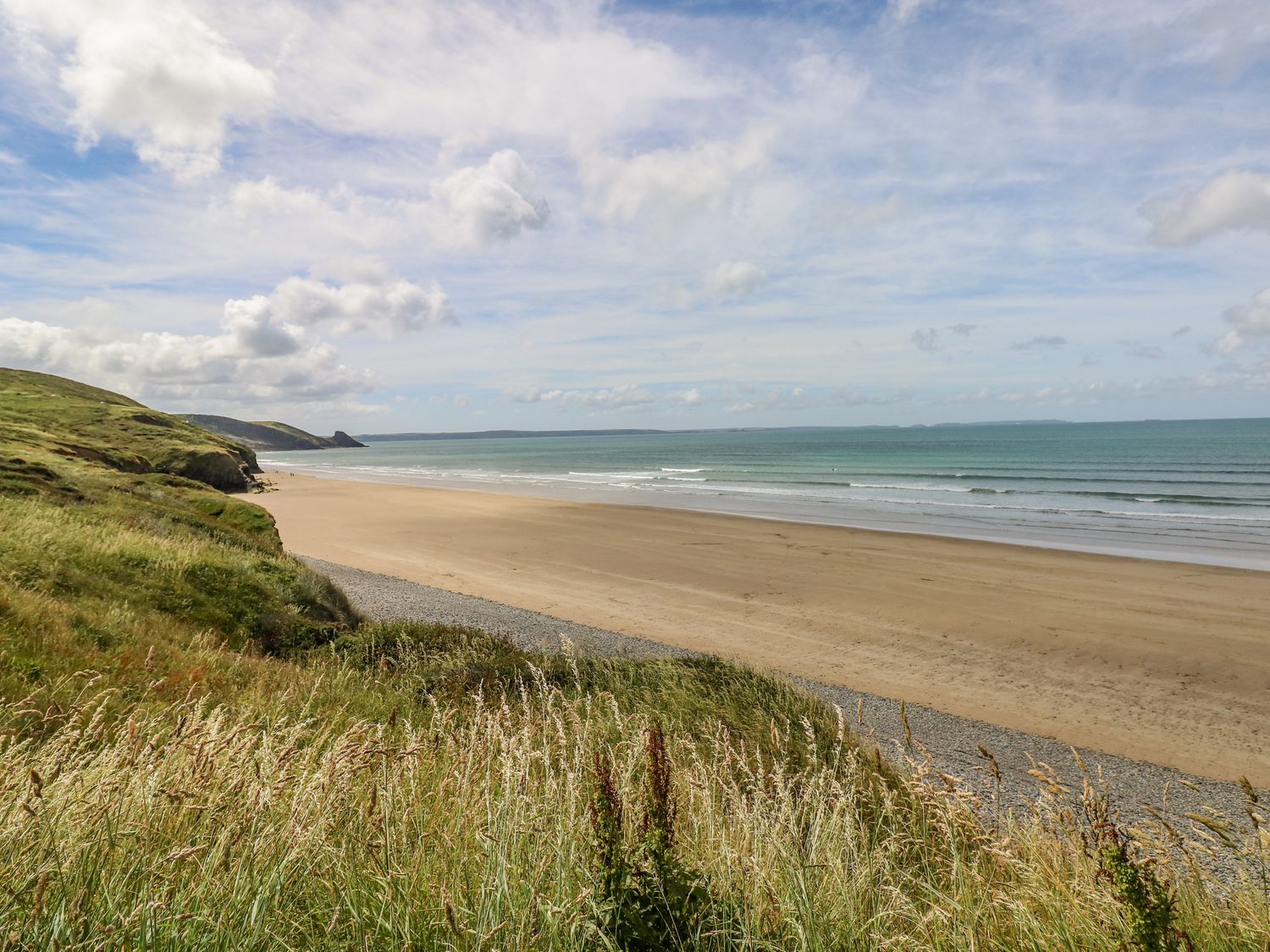 A view of a sandy beach with waves and grassy cliffs at Bay View Farmhouse in Penycwm near Solva
