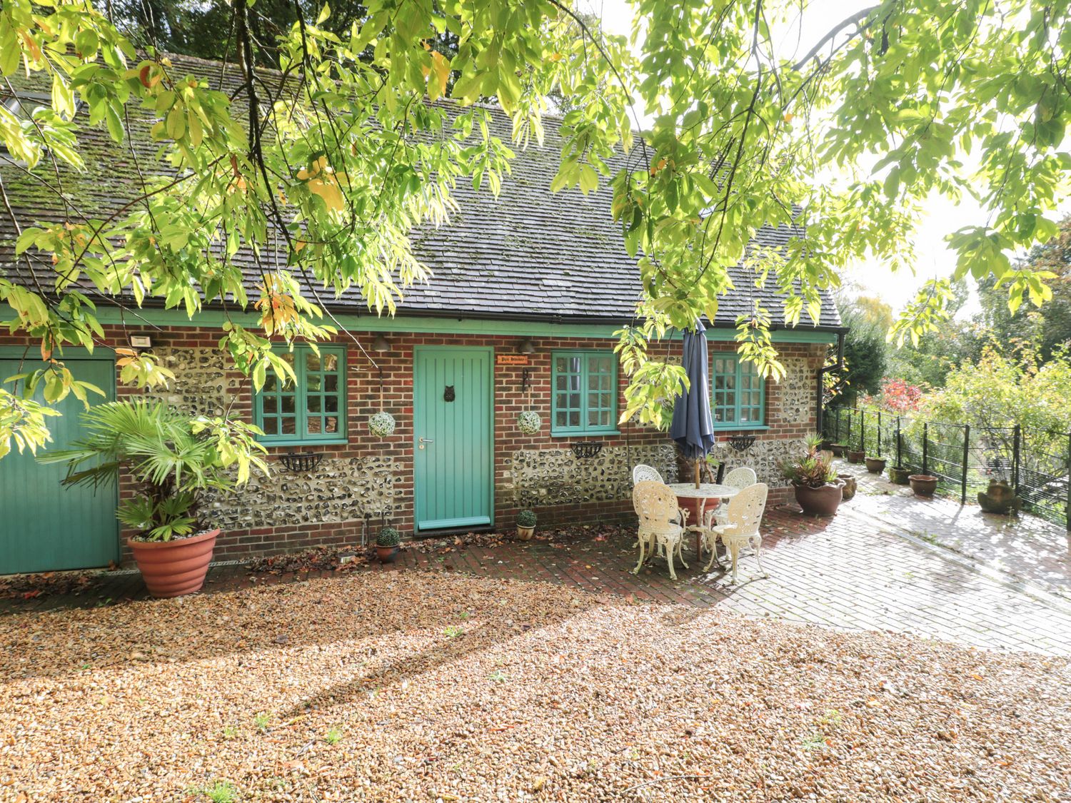 A brick and flint house with green doors and windows a small round table with four chairs and plants outside at Pips Hideaway in Milton Abbas