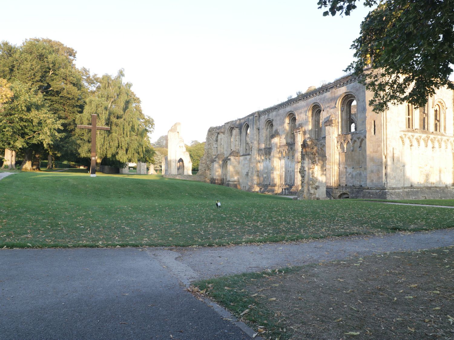 A stone building ruin with arches next to a grassy area with a wooden cross and trees at The Lodge at Crossroads Farm in Middlezoy