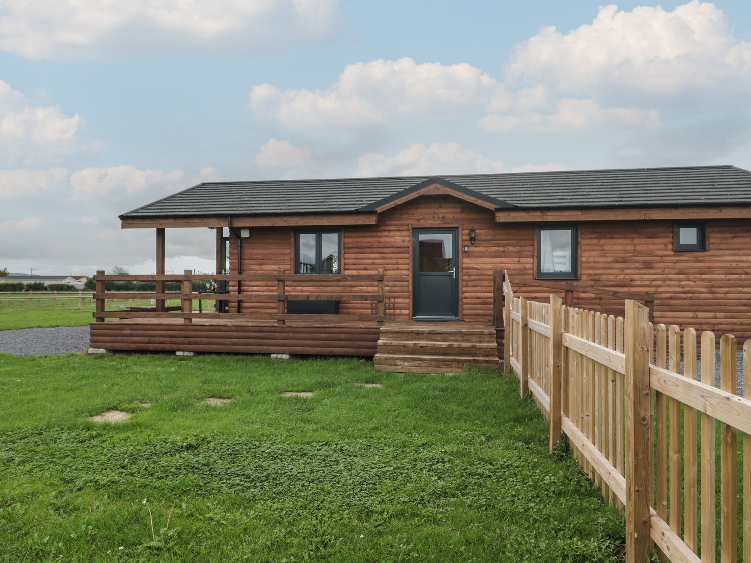 A wooden cabin with a small porch and fenced grassy yard at The Lodge at Crossroads Farm in Middlezoy