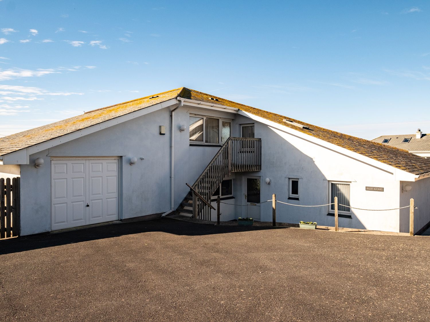 An exterior view of a white house with a sloped roof and outdoor stairs leading to a door at Blue Ridge in Polzeath