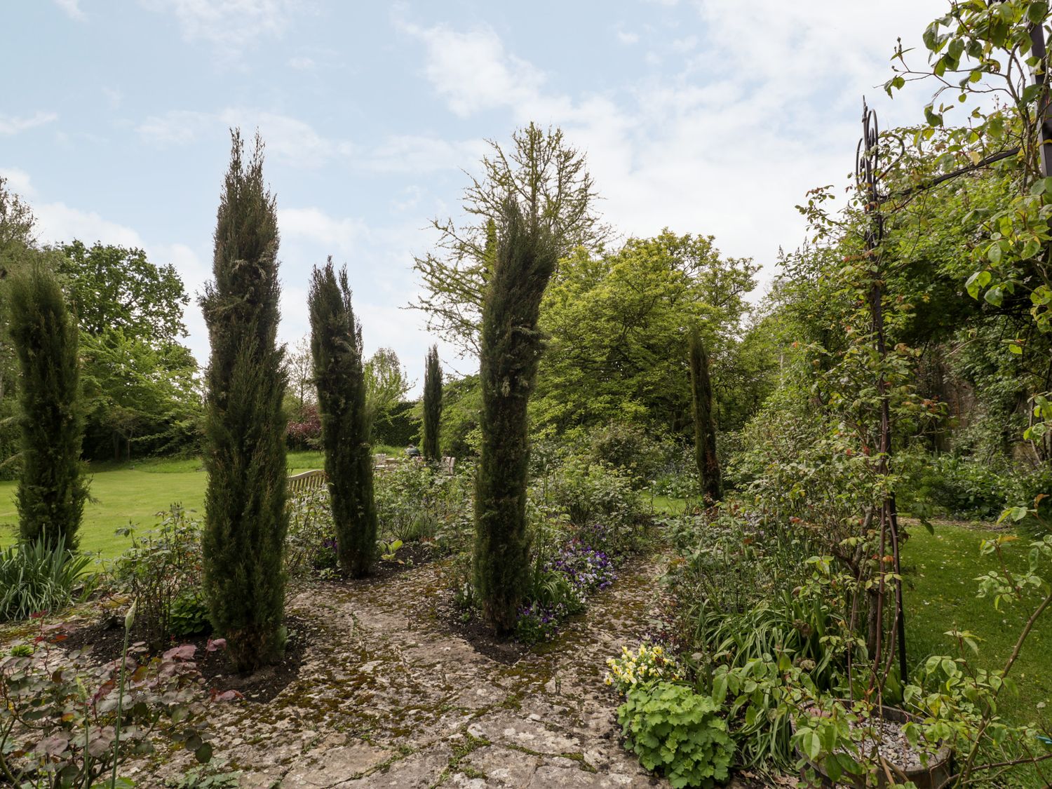 A garden with tall trees and stone pathways at Ham cottage in East Lambrook near South Petherton