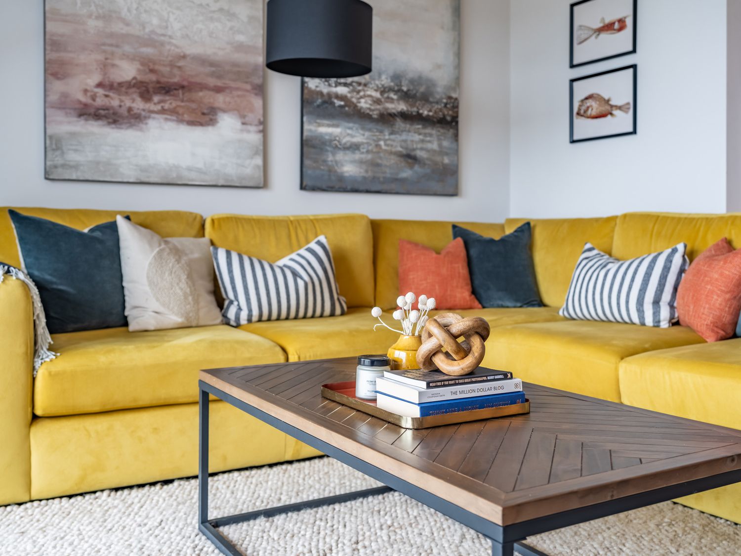 A yellow sectional sofa with various pillows and a wooden coffee table with books and decor at Porth Beach Villa in Porth near Newquay