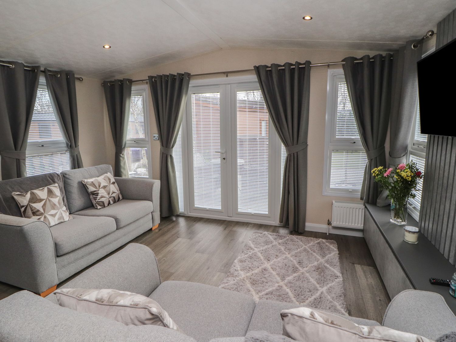 A living room with sofas pillows curtains a rug flowers on a table and a television at 24 Sherwood in Carnforth