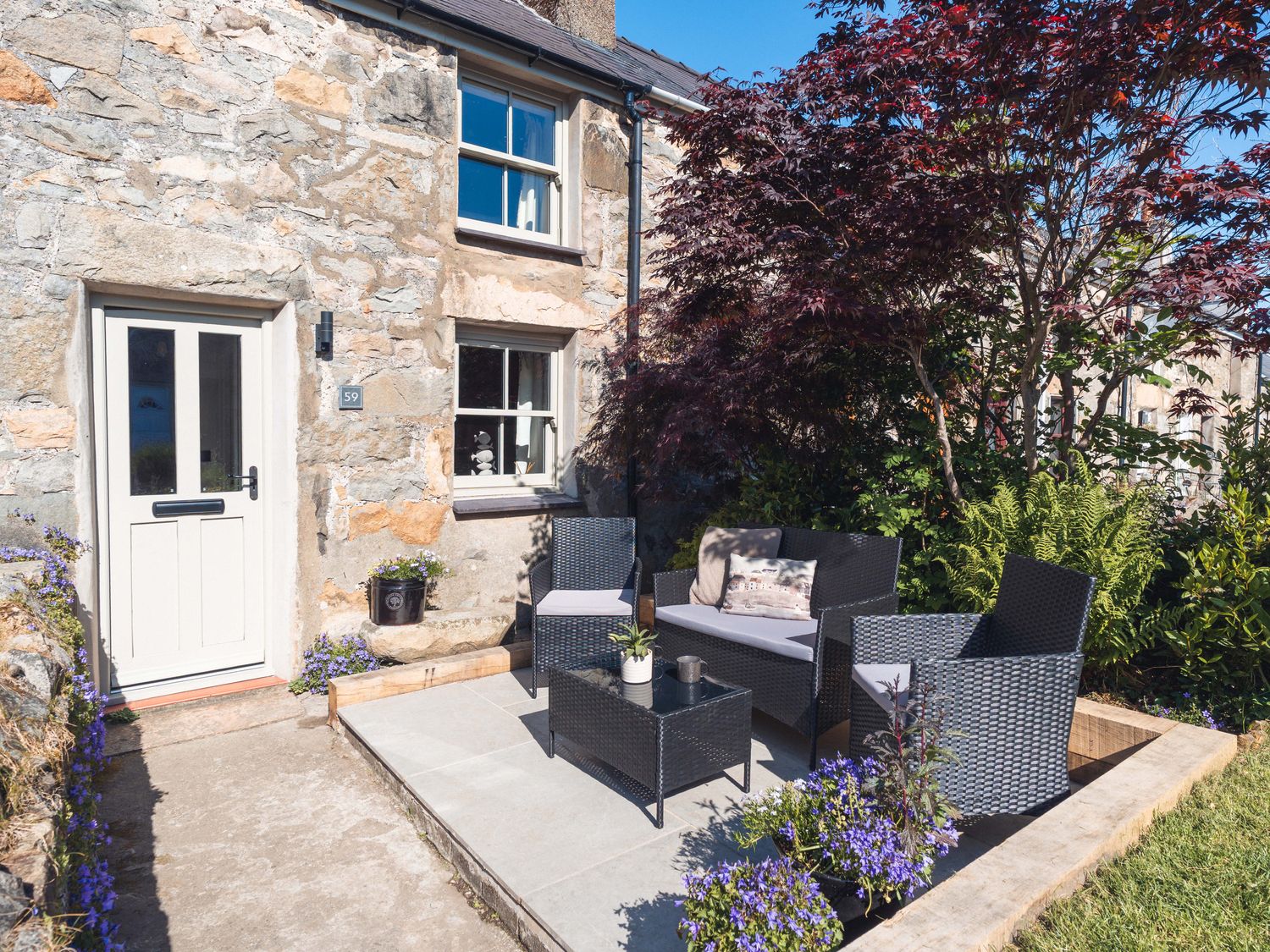 A stone house with a white door and windows and an outdoor patio with black wicker chairs and a table at Ynata in Trefor