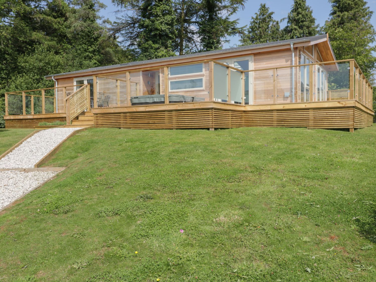 A wooden cabin with glass railings on a raised platform surrounded by grass at 2 Faraway Fields in Dobwalls