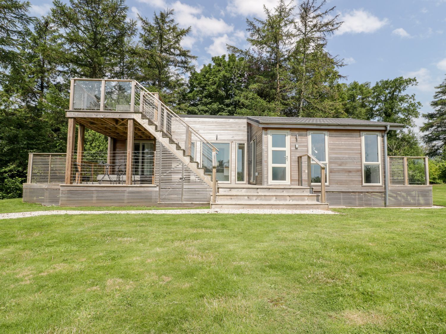 A wooden house with stairs leading to an upper deck surrounded by trees at 4 Faraway Fields in Dobwalls