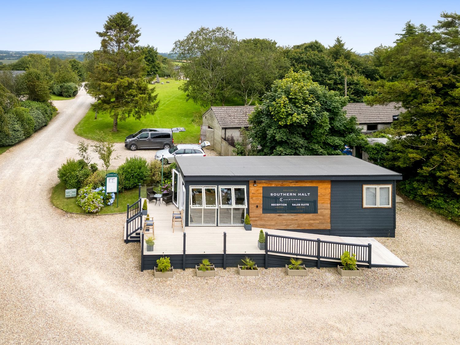 A reception and sales suite building with a ramp and outdoor seating on a gravel driveway surrounded by trees at 4 Faraway Fields in Dobwalls