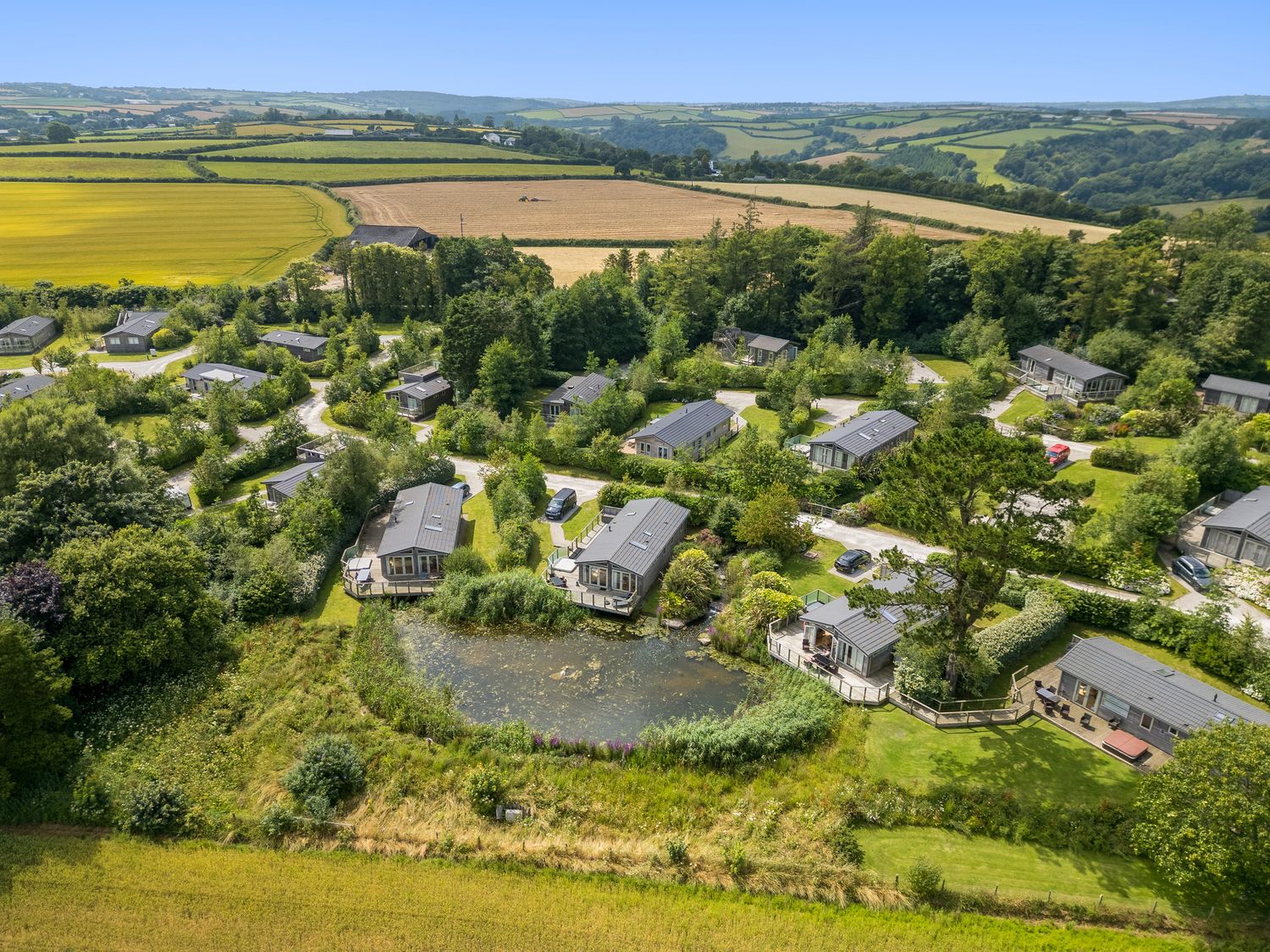 A cluster of houses surrounded by trees and a pond in a rural area at 5 Meadow Retreat in Dobwalls