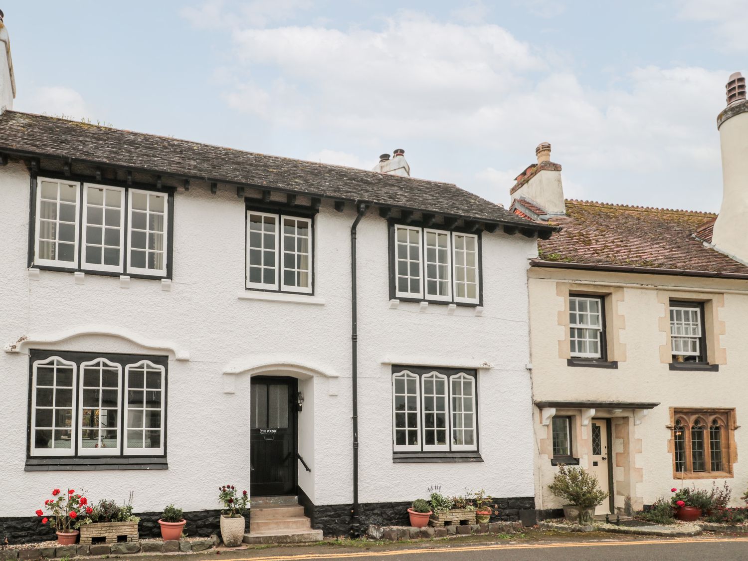 A street view of two adjoining houses with multiple windows and flower pots at The Pound in Porlock