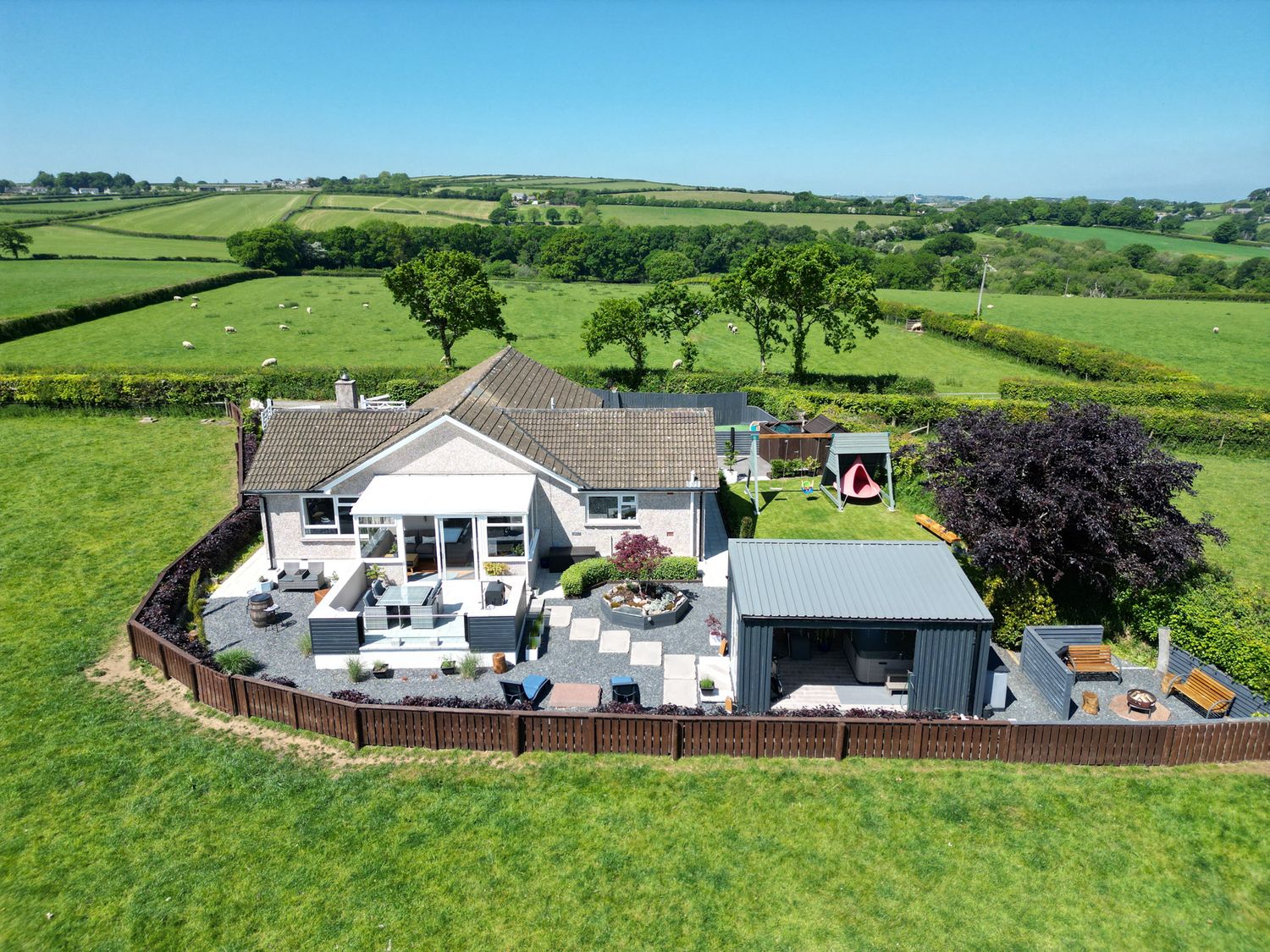 An aerial view of a fenced house with patios play area and garden furniture in the countryside at Ashlea Launceston