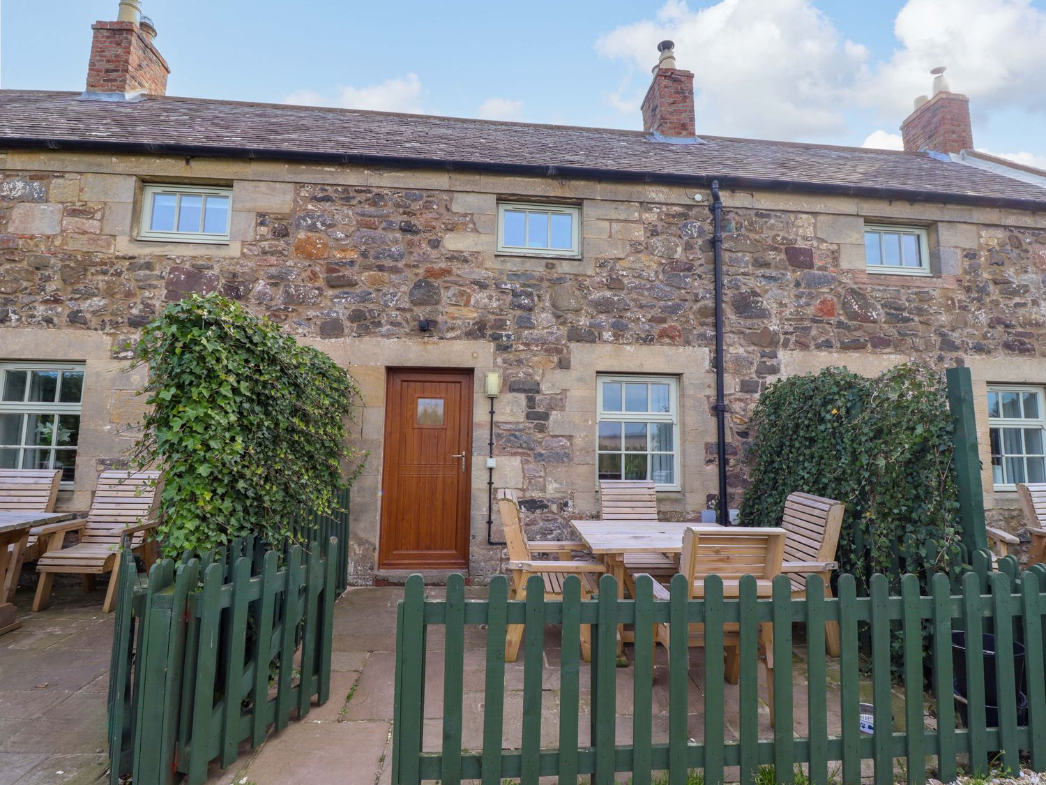 An outdoor area with wooden furniture and stone wall at Heather Cottages - Grayling in Bamburgh