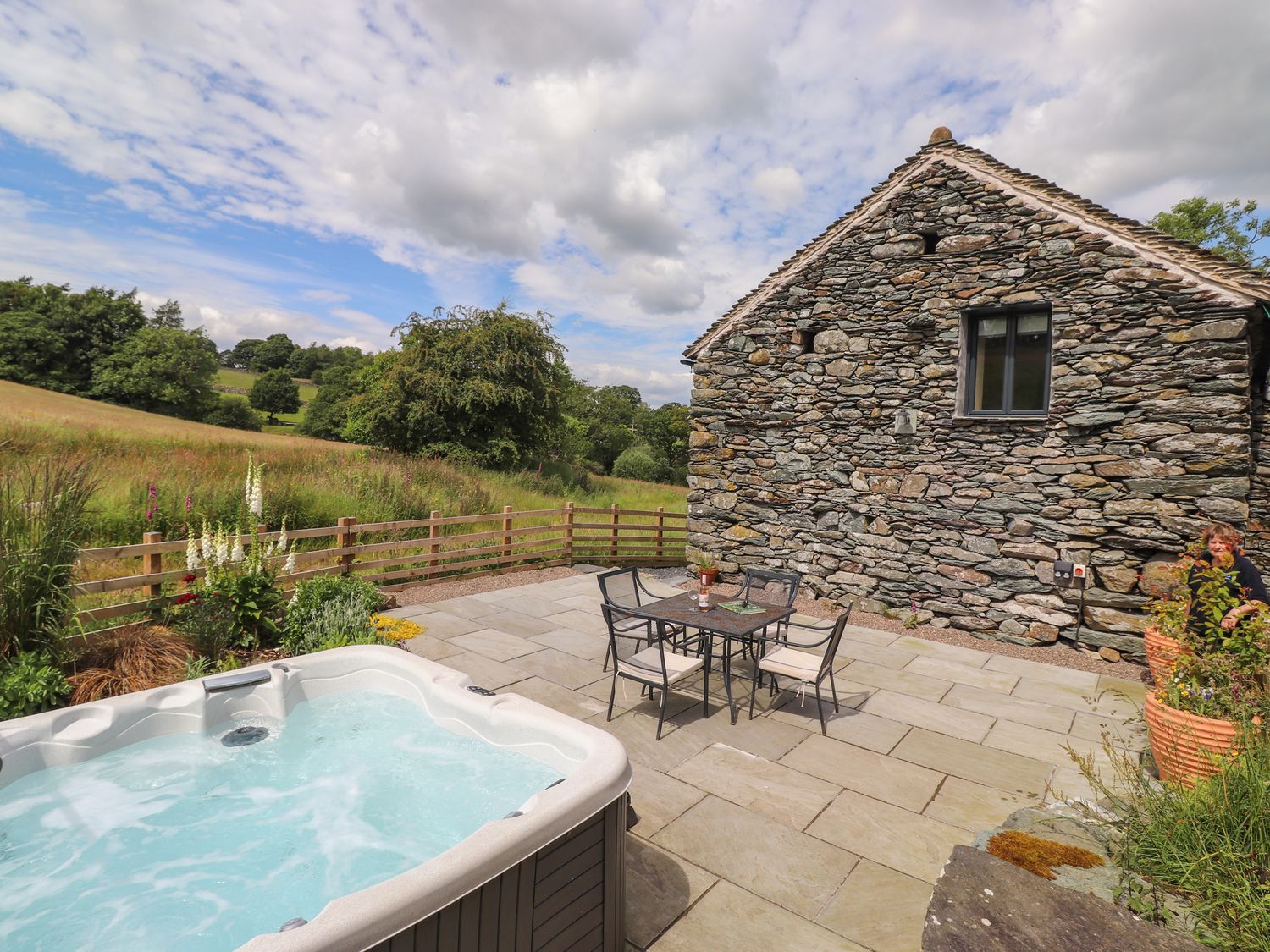 An outdoor patio area with a hot tub table and chairs stone building and green fields at Meadow Syke Barn in Bampton Cumbria