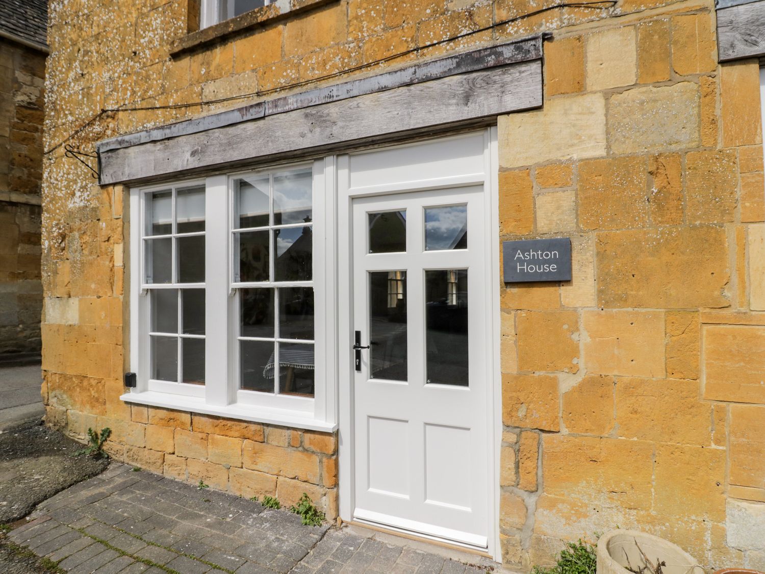 A white door and window on a stone building with a sign reading Ashton House in Blockley