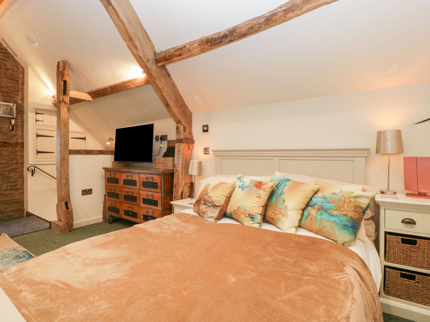 A bedroom with a bed pillows a wooden dresser television and exposed ceiling beams at Palace Studio in St Weonards