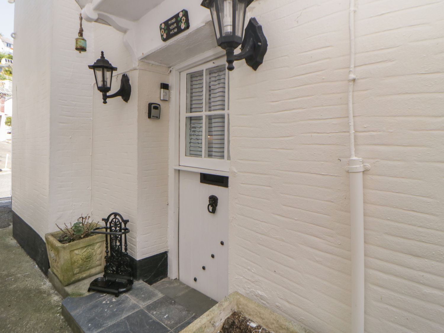 A small white cottage door with two black outdoor lanterns and a planter box beside it at Alexandra Cottage in Looe