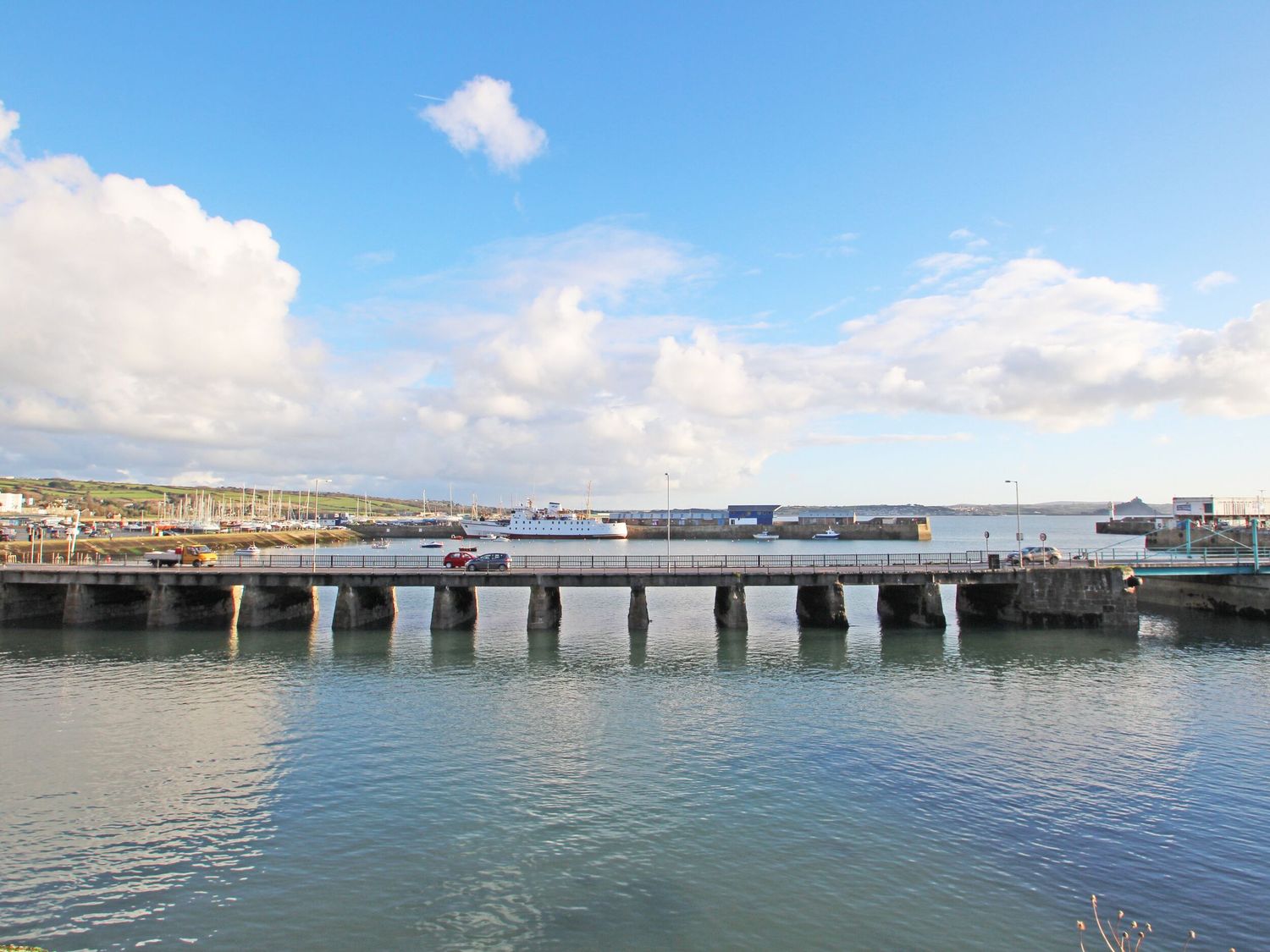 A stone bridge over water with cars and boats in the background at The Old Piggeries in Gulval near Penzance