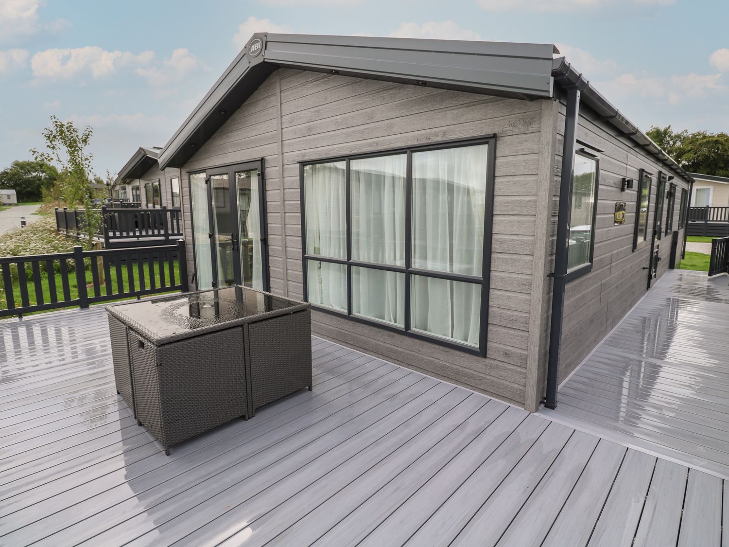 An outdoor deck area with a wicker table and a modern gray cabin at Penmarlam Lodge Retreat 12 in Bodinnick