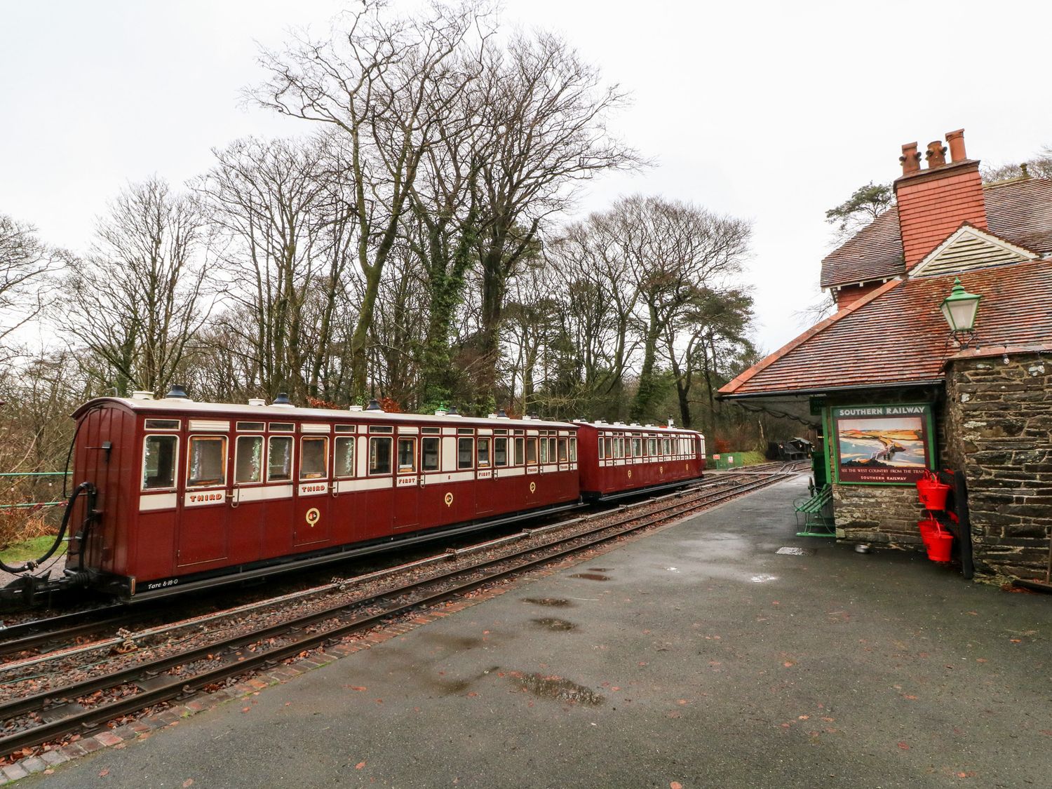 A vintage train at a small railway station with a stone building and trees in the background at Springside in Woody Bay near Lynton