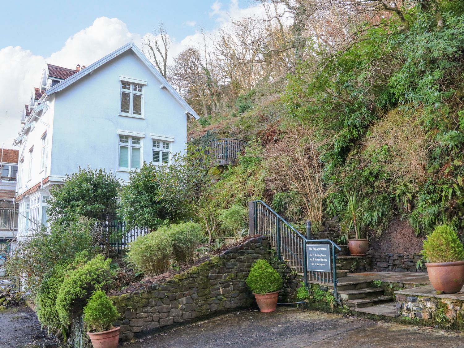 A white multi-story house next to a stone staircase with potted plants and greenery at Springside in Woody Bay near Lynton